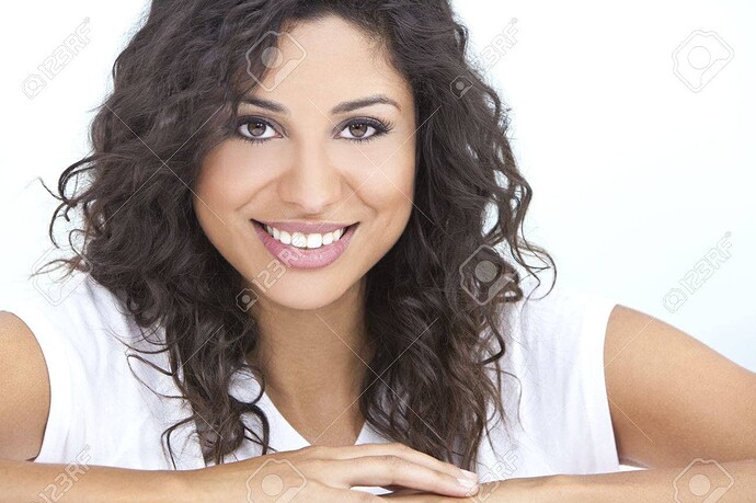 Una donna sorridente con capelli ricci scuri e una maglietta bianca appoggiata con le braccia su una superficie bianca. (Didascalia da IA)